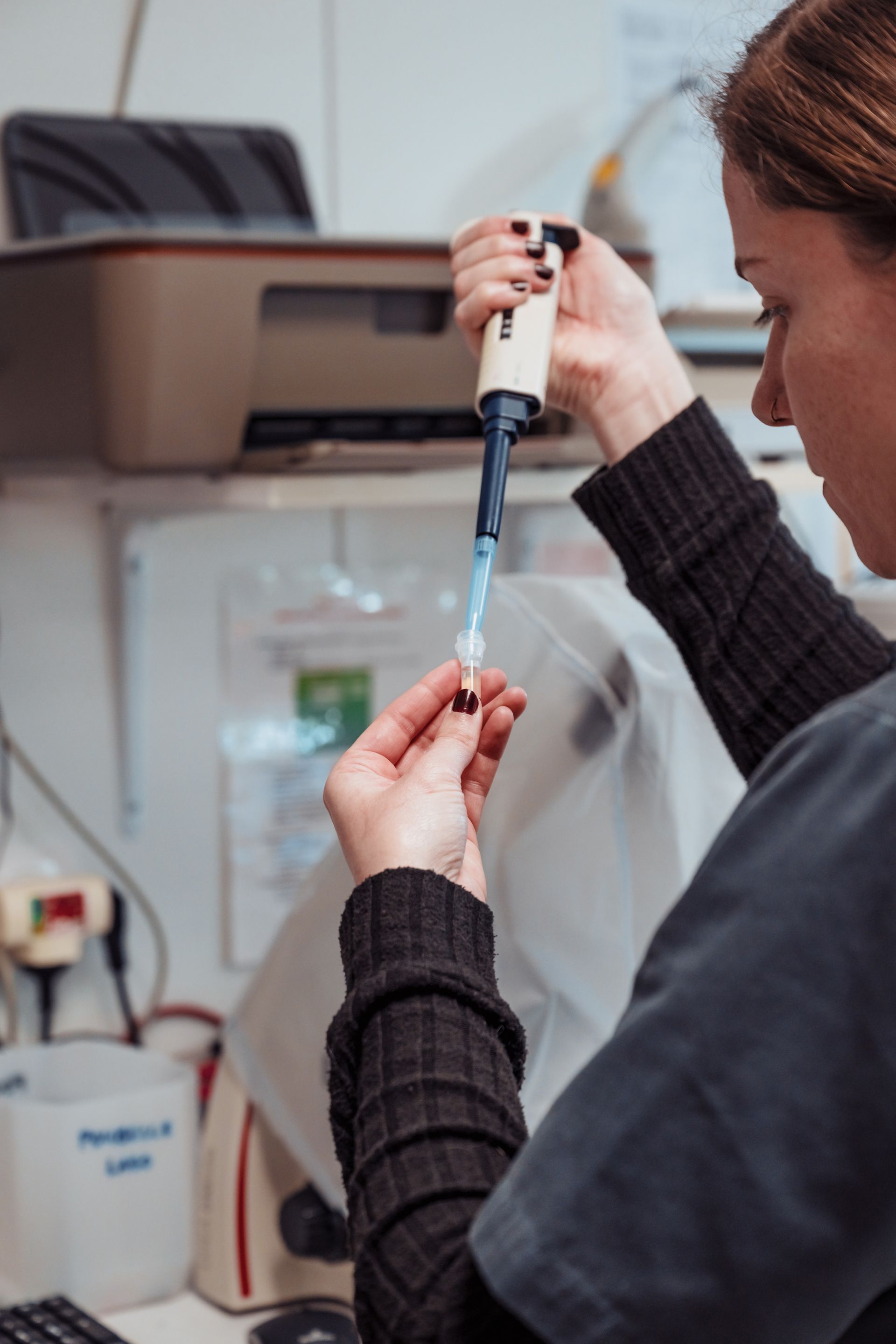 Femme utilisant une pipette dans un laboratoire, tenant un petit flacon.