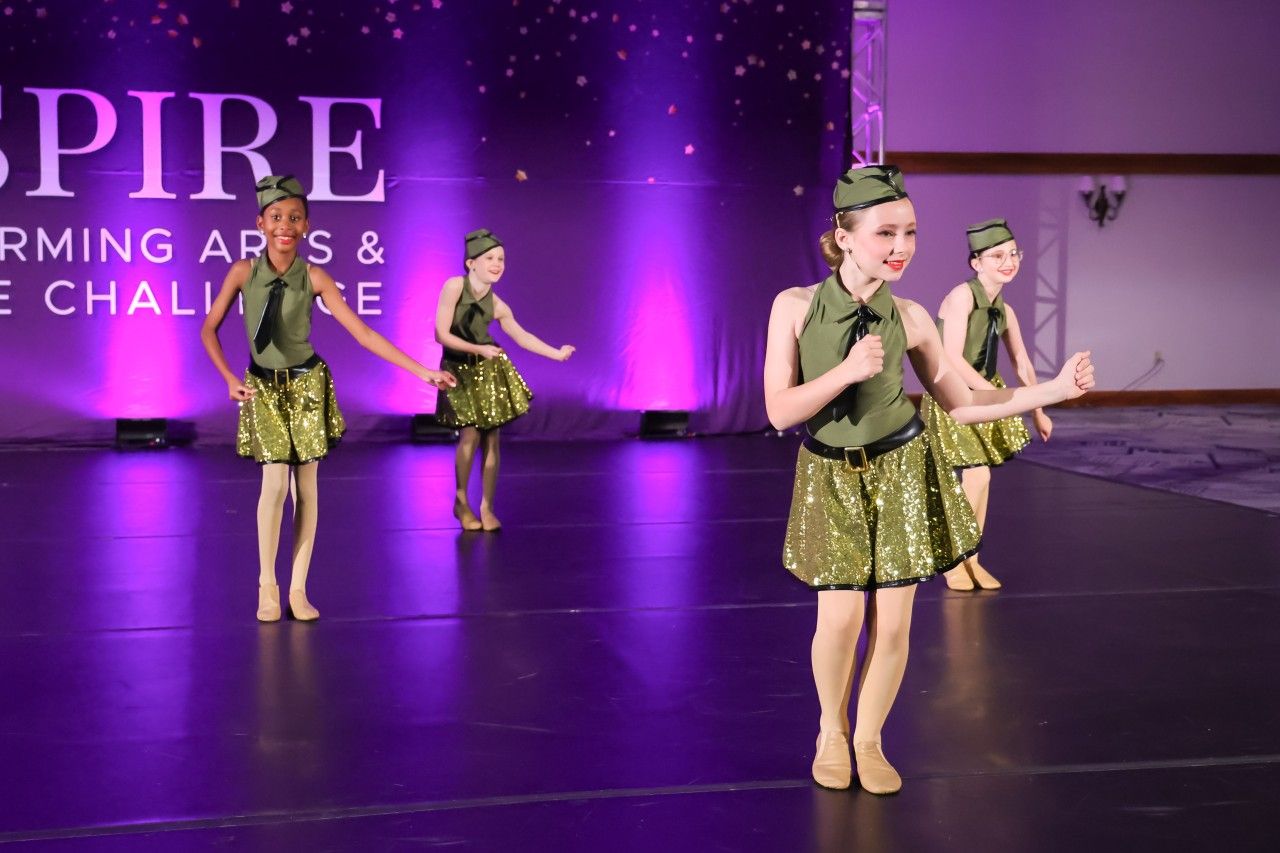 Four young dancers in green sequined costumes perform on a purple-lit stage