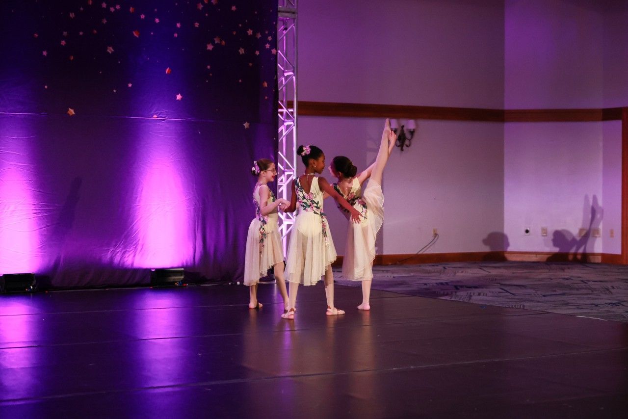 Three dancers in white perform on a purple-lit stage with a starry backdrop