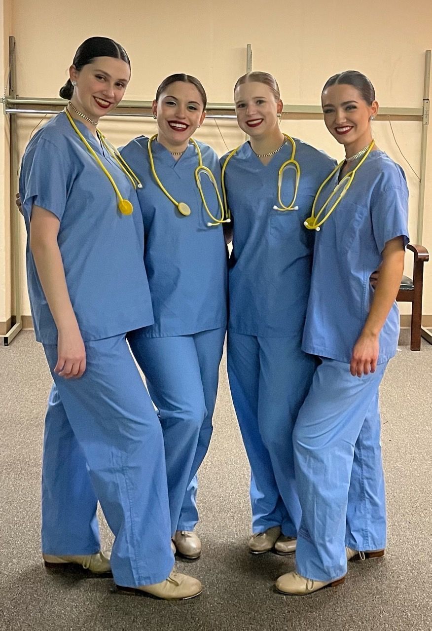 Four people in blue medical scrubs with stethoscopes, standing together and smiling indoors.