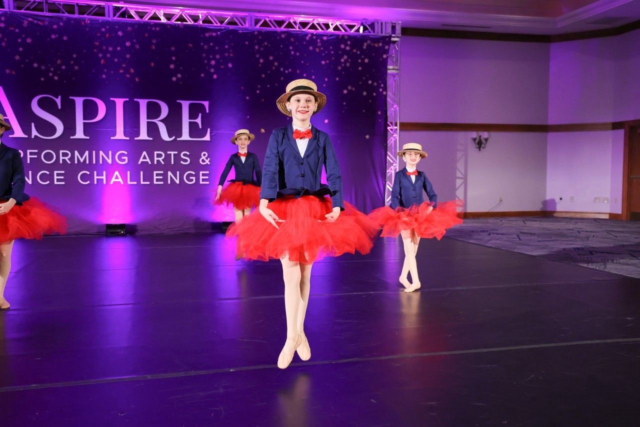 Two dancers in red tutus perform on a purple-lit stage at an Aspire performing arts dance challenge