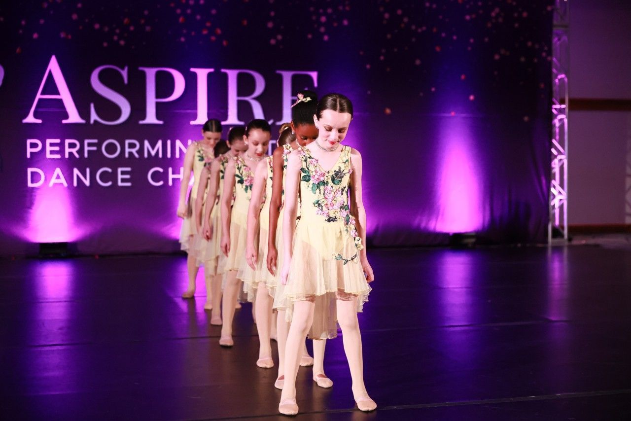Dance team in cream outfits performing on a purple-lit stage with “ASPIRE” backdrop.