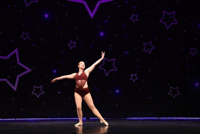 Dancer in maroon costume striking a pose on a stage with purple starry lights