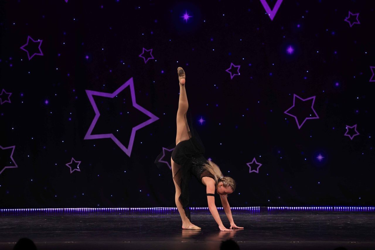Dancer balancing in a one-handed split pose on a stage with purple starry backdrop