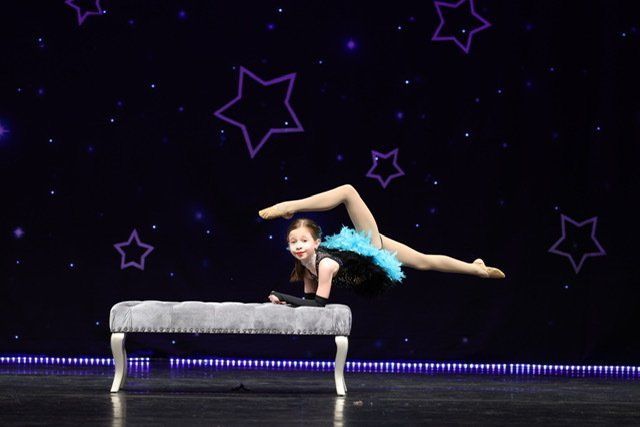 Contortionist in a blue costume balancing on a bench against a starry purple stage backdrop