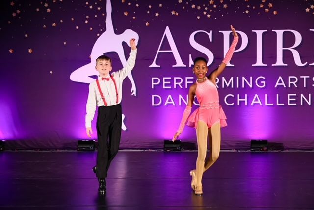 Two dancers on stage under purple lights, performing at the Aspire Performing Arts Dance Challenge.