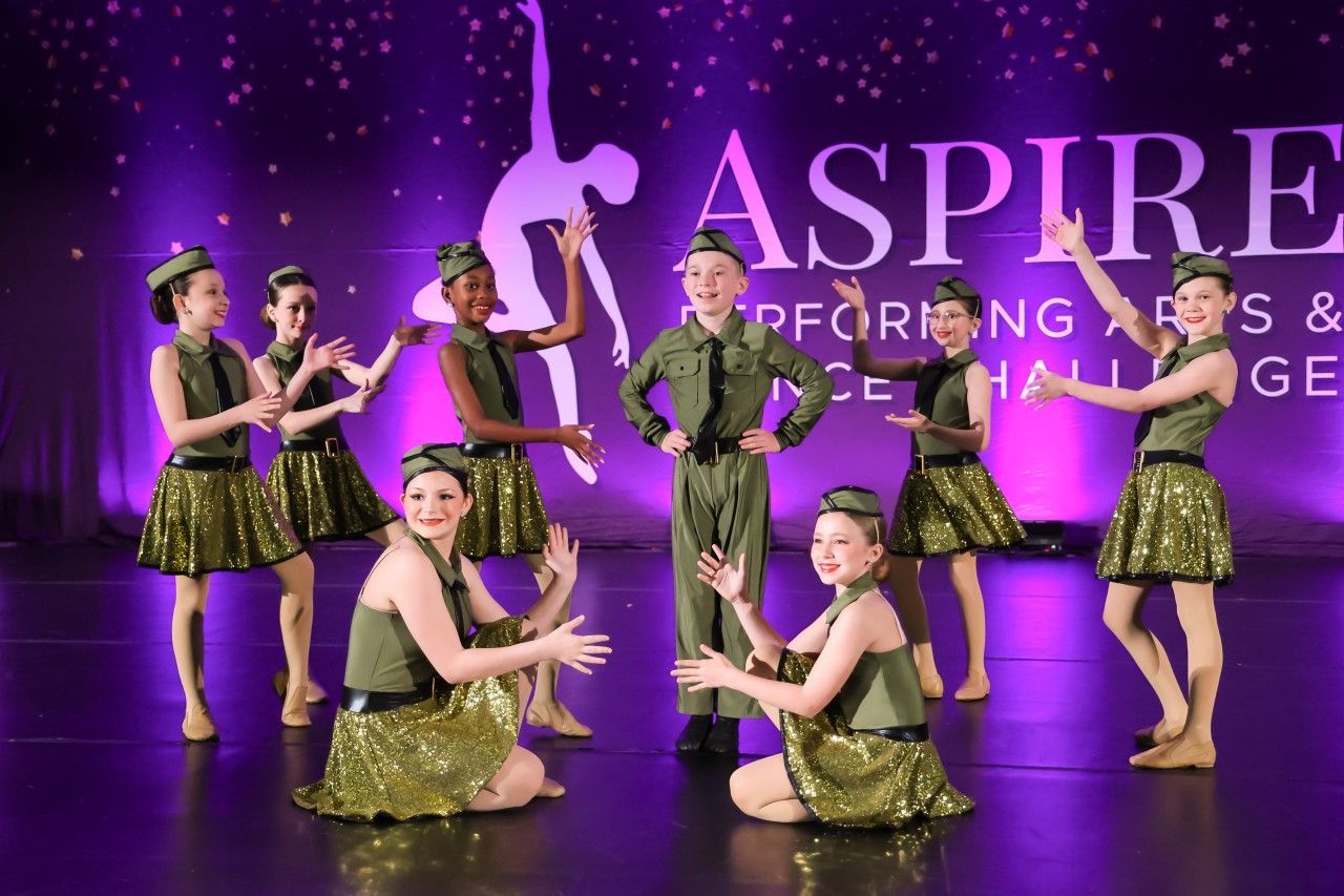 Dance team performing on a purple-lit stage with gold costumes and a large “ASPIRE” backdrop
