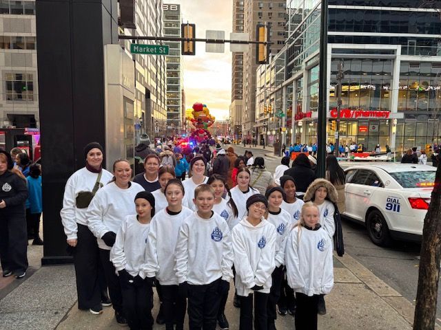 Group marching in white jackets down a city street with police cars and buildings nearby