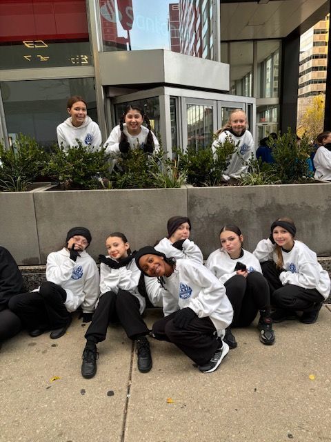 Group of people in white jackets posing outdoors in front of a building planter