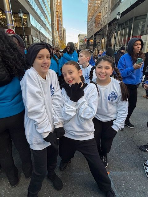 Three youths in white hoodies pose smiling in a city street parade line