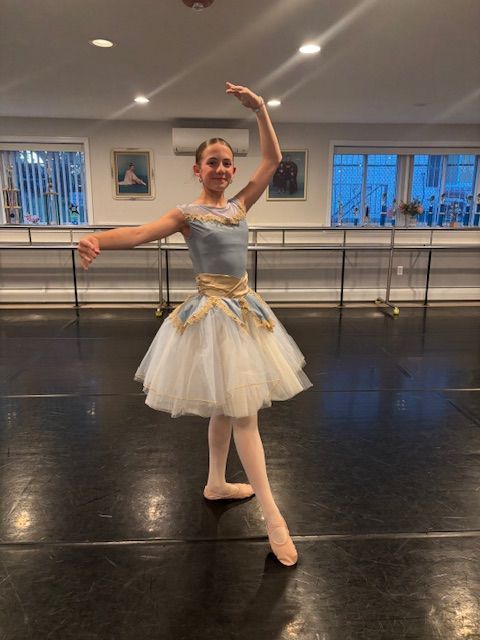 Ballet dancer in a white and gold tutu poses in a studio with ballet barres and mirrors.