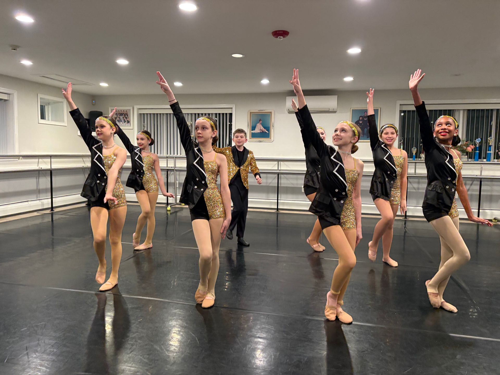 Dance team in black and gold costumes posing with arms raised in a studio mirror room