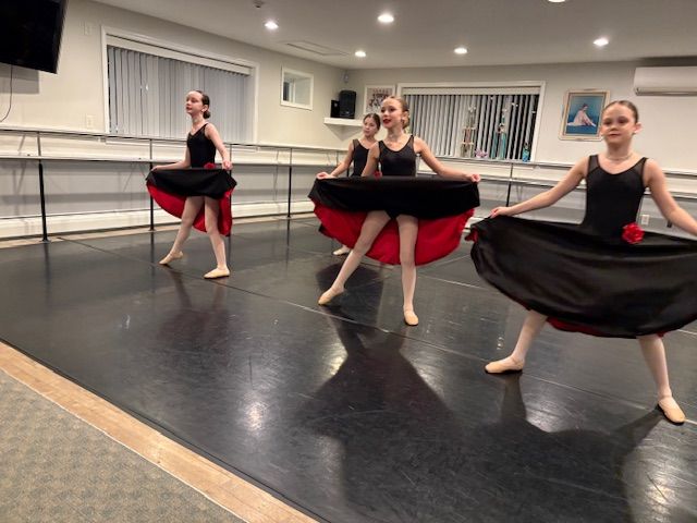 Three dancers in black and red skirts posing in a ballet studio