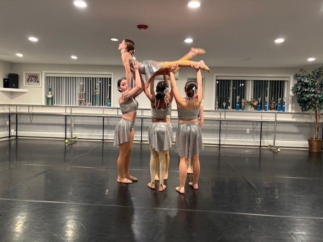Four dancers practicing a lifted pose in a studio with ballet barres and mirrors