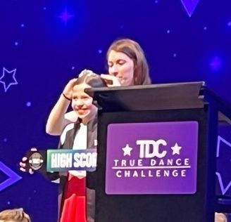 Woman and child at a podium labeled “TDC True Dance Challenge” on a purple stage backdrop