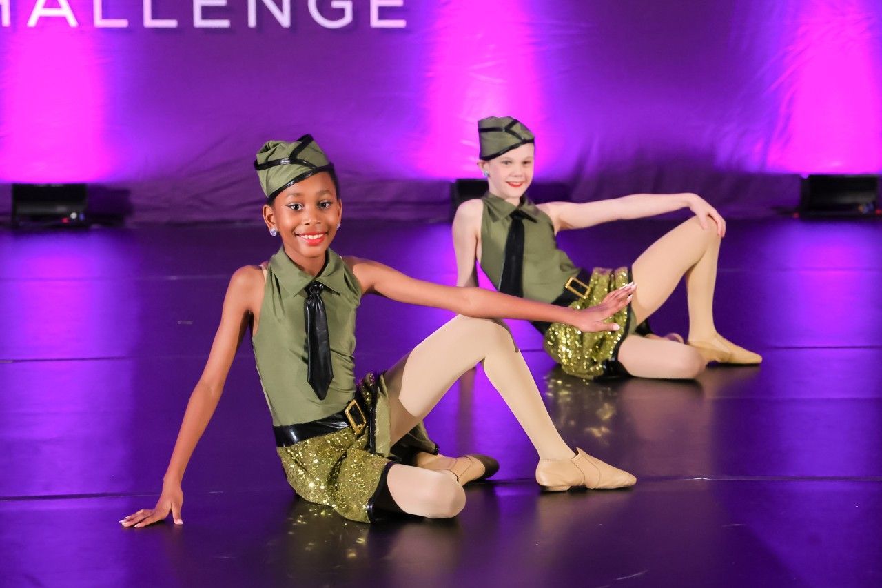 Two dancers in green costumes pose on a purple-lit stage during a performance