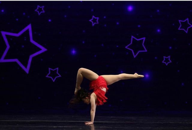 Dancer balancing on one hand in a red costume against a dark purple starry stage backdrop