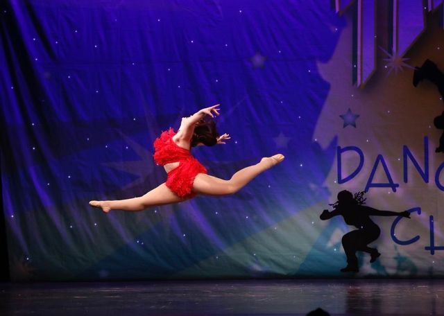 Dancer in red leaps across a lit stage with a purple backdrop and starry decorations