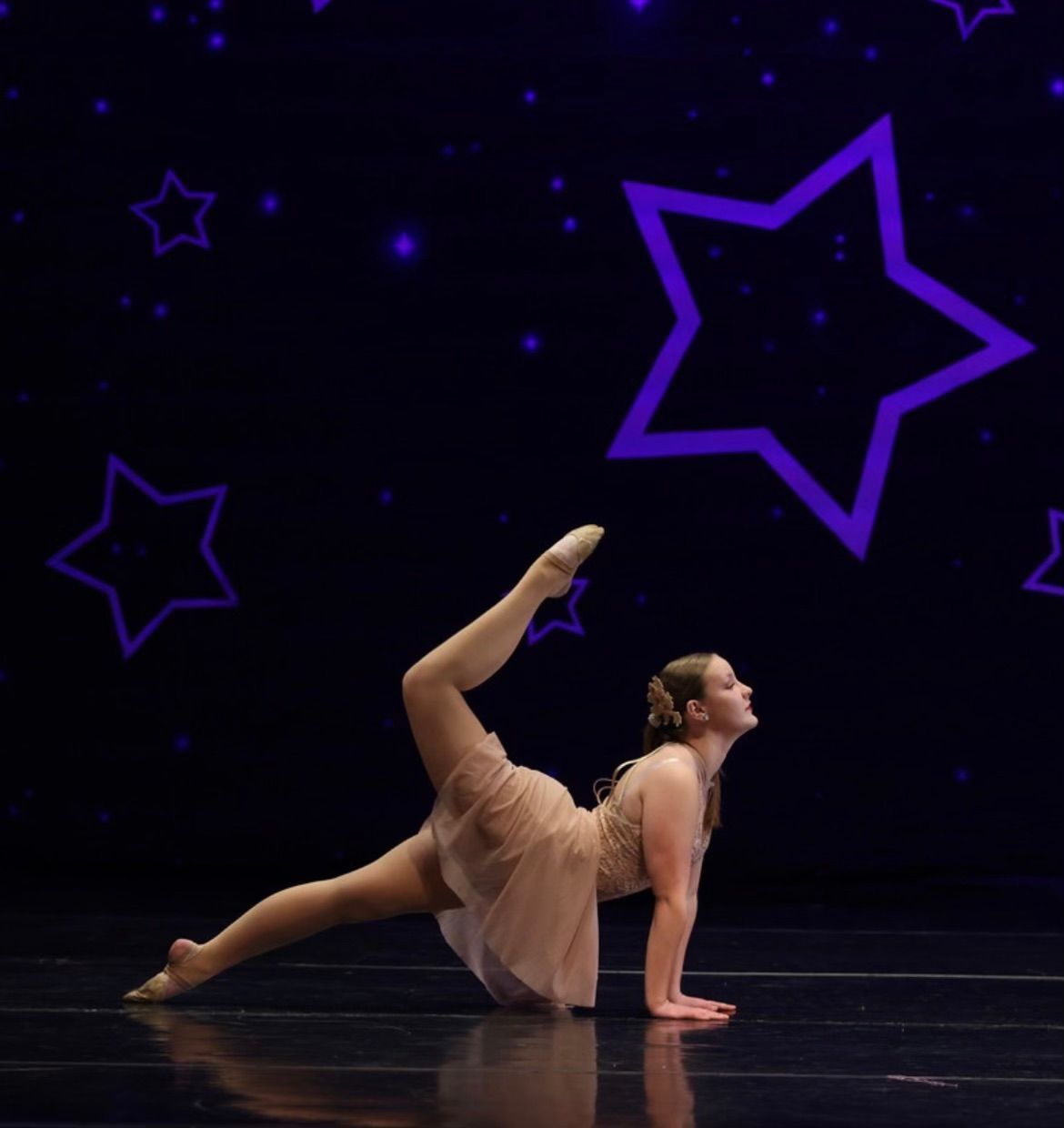 Dancer in a peach dress posing onstage under purple star outlines