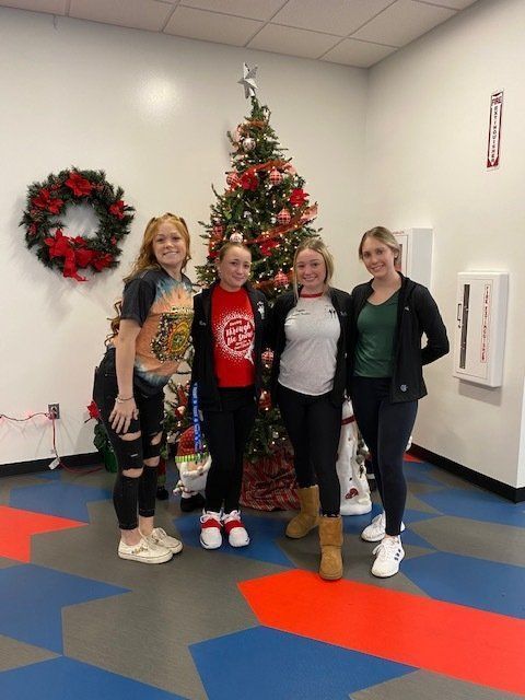 Five people posing by a decorated Christmas tree in a lobby with wreaths and red-blue floor tiles