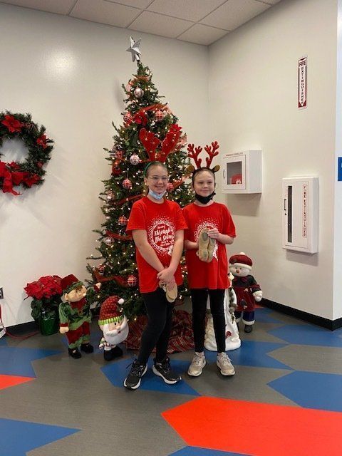 Two people in red shirts pose by a decorated Christmas tree in a festive lobby