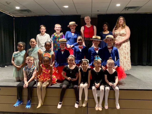 A group of children and adults in colorful costumes posing on stage for a performance photo.