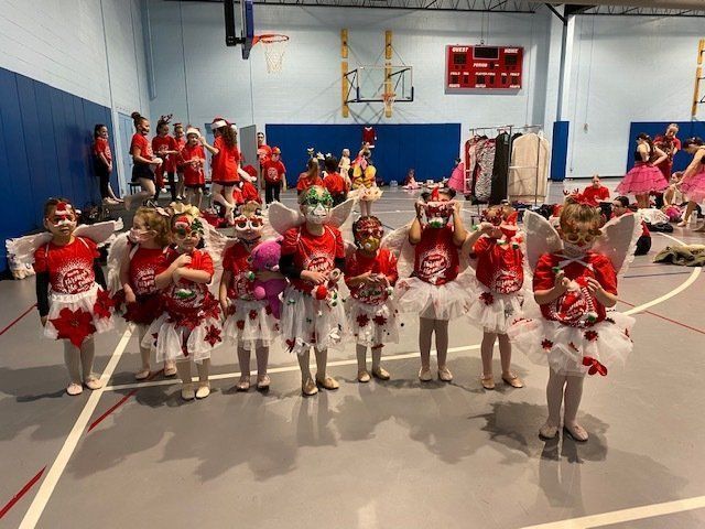 Children in red-and-white costumes stand in a gym for a dance performance.