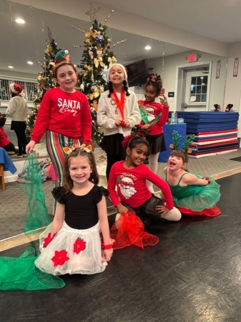 Children in holiday costumes posing in front of Christmas trees, smiling on a dance floor