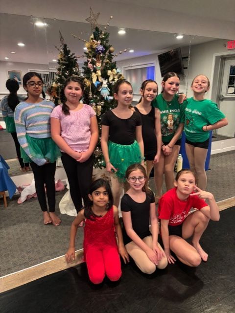 Group of children posing indoors in front of a decorated Christmas tree.
