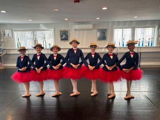 Six dancers in navy and red costumes pose in a bright studio, standing in a line.