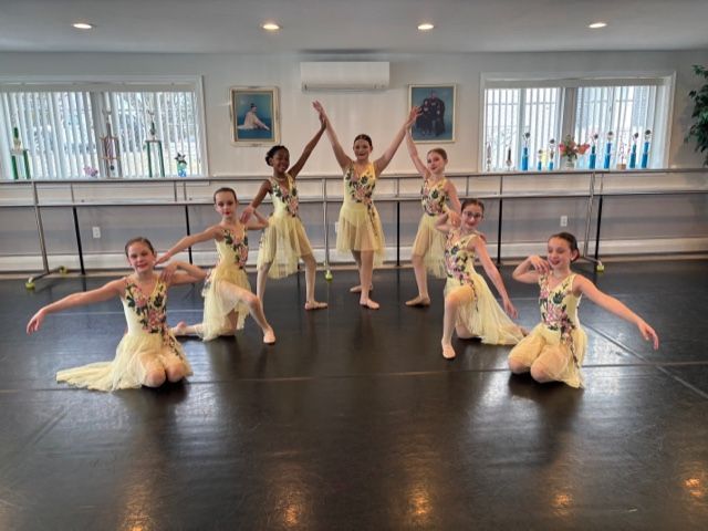 Young dancers in yellow costumes pose in a ballet studio with mirrors and barres