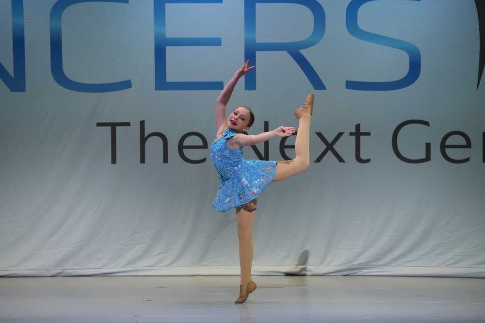 Young dancer in a blue dress performing a high leg extension on stage