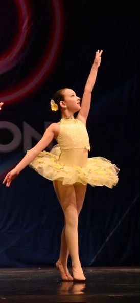 Ballet dancer in a pale yellow tutu posing on stage with one arm raised