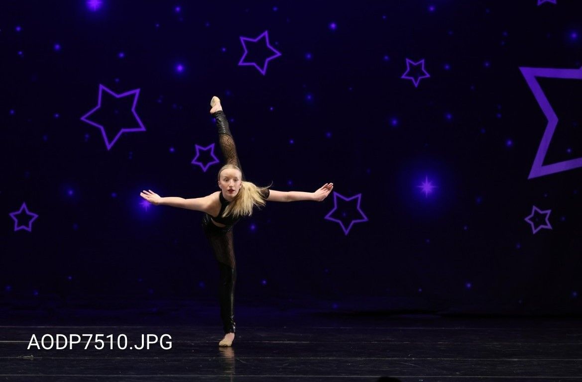 Young dancer balancing on one leg with arms outstretched on a dark purple stage with star patterns