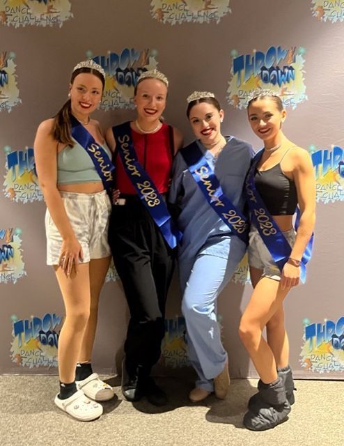 Four dancers posing with medals and sashes in front of a colorful backdrop.