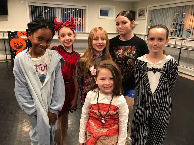 Six children posing indoors in Halloween costumes, including a clown, vampire, and striped suit.