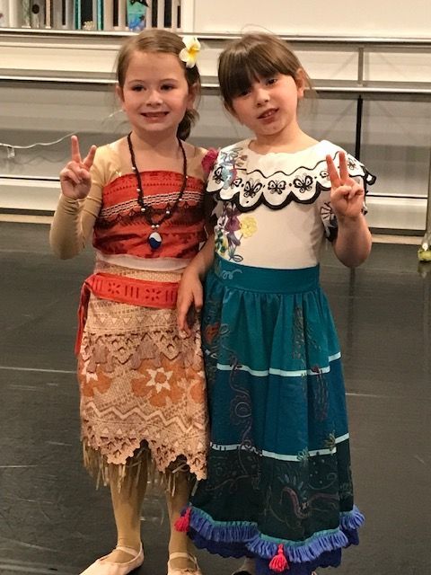 Two children posing and smiling in colorful traditional-style dresses, each holding up a peace sign.