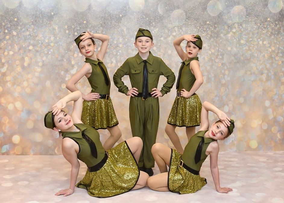 Five children in olive green dance costumes pose against a sparkling gold backdrop.