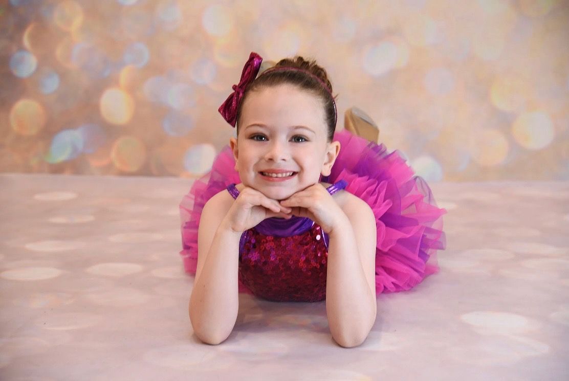 Smiling child in a pink tutu resting on hands against a soft bokeh backdrop