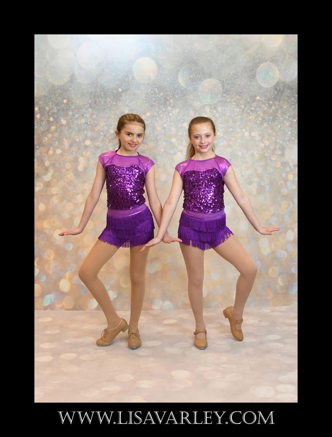 Two dancers in matching purple costumes pose against a glittery backdrop