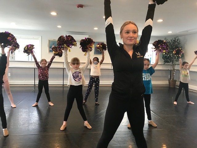Dance class with instructor and children holding purple pom-poms in a studio