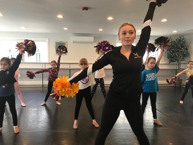 Dance class practice with instructor and children holding pom-poms in a studio