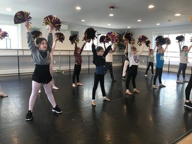 Cheerleaders rehearsing in a dance studio, holding pom-poms overhead in rows.