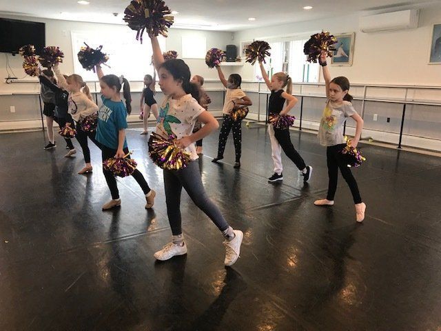 Group dance class practicing with pom-poms in a mirrored studio
