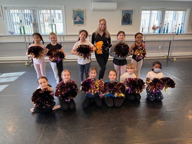 Children holding black and gold pom-poms pose in two rows in a dance studio.