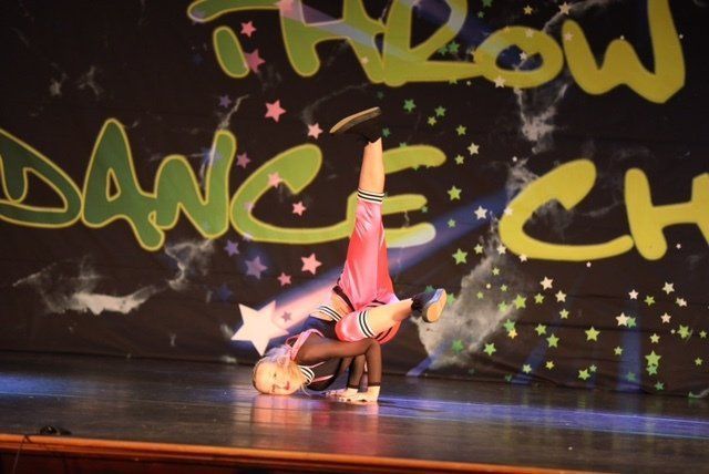 Dancer in pink outfit doing a one-handed handstand on a stage with graffiti-style backdrop and stars