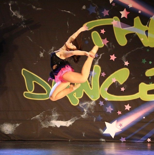 Contortionist in pink and black costume mid-air on a dance stage with colorful graffiti backdrop