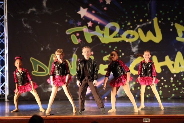 Children performing a dance onstage in pink and black costumes against a starry backdrop