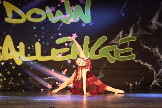 Dancer in red costume holding a split pose on stage beneath “Down Challenge” backdrop