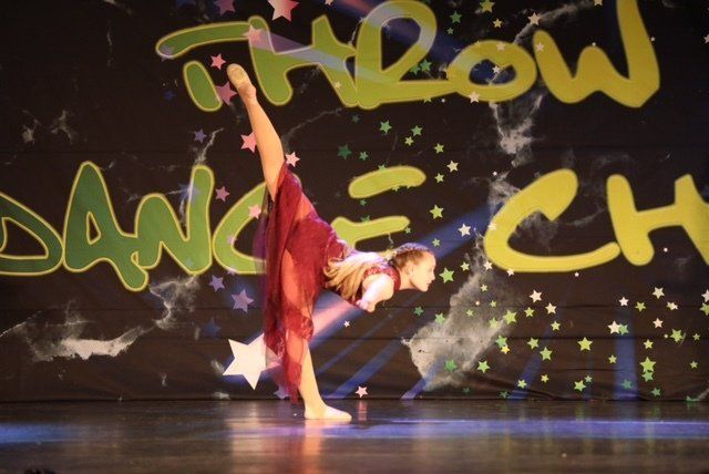 Dancer in red costume holds a split pose onstage before a graffiti-style backdrop